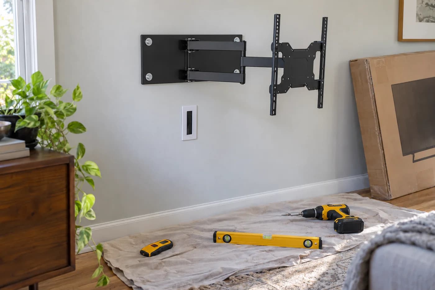 Articulating TV mount bracket fastened to a wall with a level, stud finder and cable plate below it